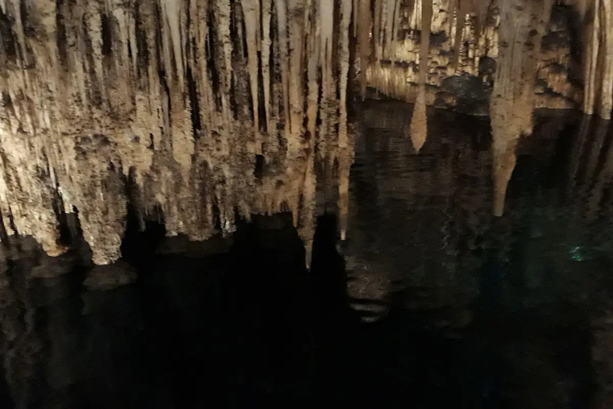 Stalactites hanging over the still dark water of Lake Martel, their points reflected in the lake.